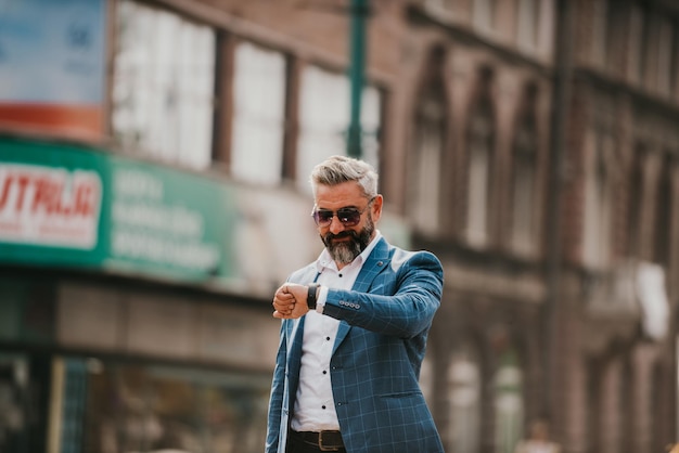 Senior businessman walking in the city carrying a bag and using a watch