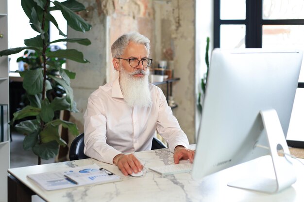 Photo senior businessman with a stylish beard working on computer at his office desk