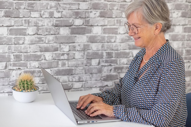 Senior businesswoman typing on laptop keyboard sitting at desk elderly lady smiling online computer