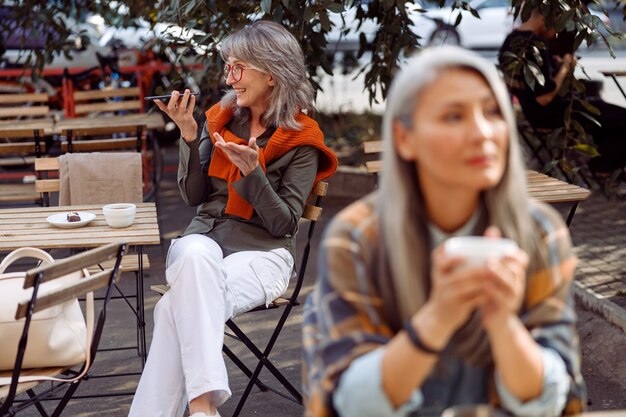 Senior cafe guests focus on silver haired woman with glasses recording audio message