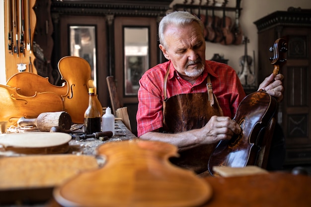 Senior carpenter craftsman polishing violin instrument in his carpenter's workshop.