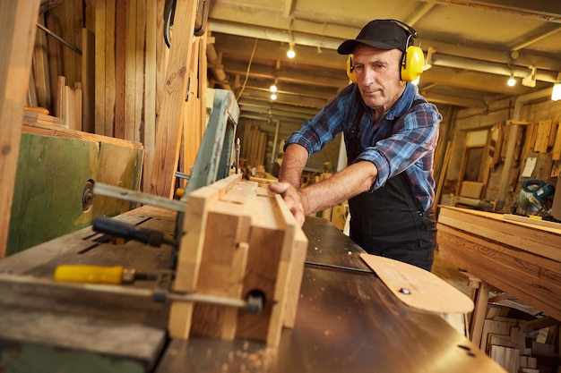 Senior carpenter in uniform works on a woodworking machine at the carpentry manufacturing