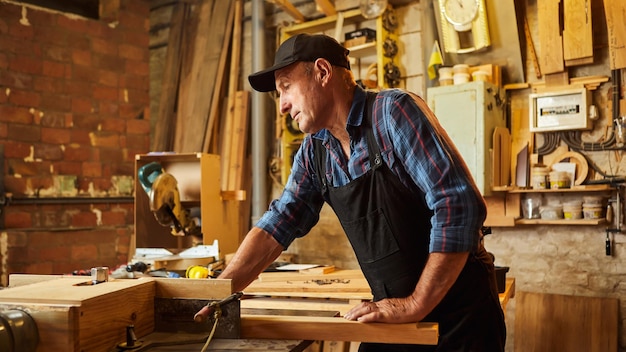 Senior carpenter in uniform works on a woodworking machine at the carpentry manufacturing