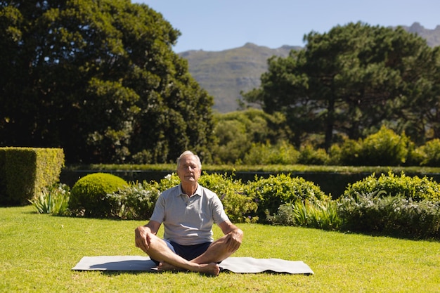 Senior caucasian man practicing yoga, meditating in sunny garden. retirement retreat and active senior lifestyle concept.