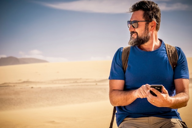 Senior caucasian nice man with beard uses cellular phone in the desert dunes