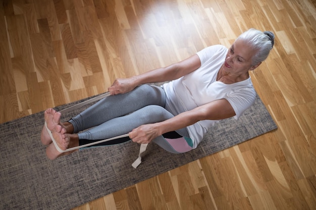 Senior caucasian woman doing abs exercises sitting in boat yoga pose at home