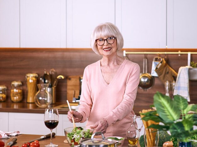 senior cheerful woman is cooking at modern kitchen