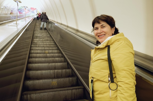 Senior citizen brunette woman in a jacket rides up the escalator in the subway