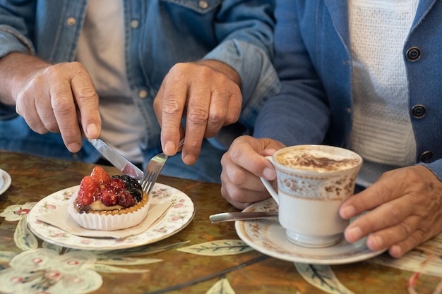 Senior couple having breakfast at coffee shop with a small fresh fruit cake and cup of cappuccino in artistic ceramic mug