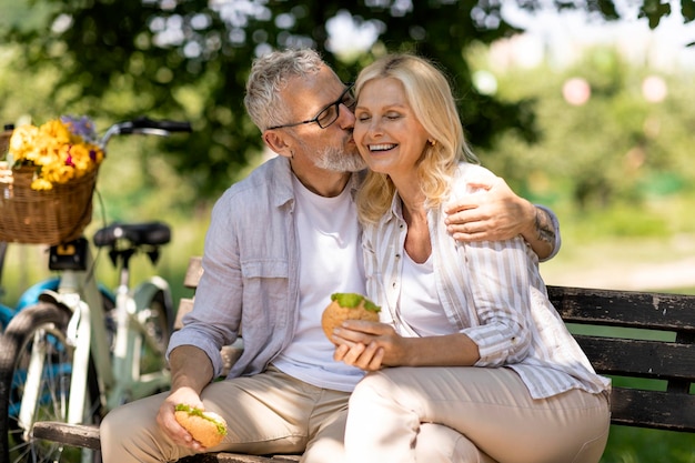 Senior couple having lunch break outdoors while sitting on bench in park