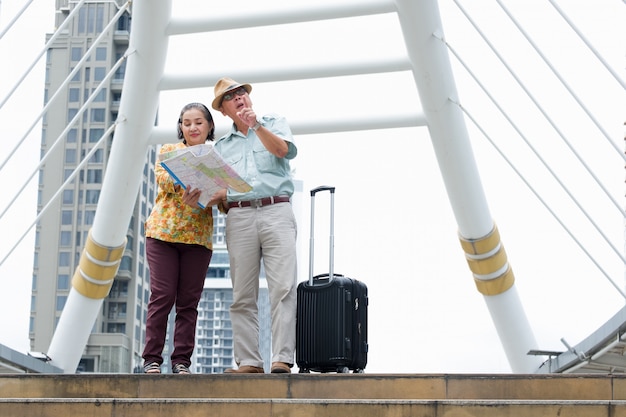 Senior couple is standing holding the map to search for destinations on the streets.