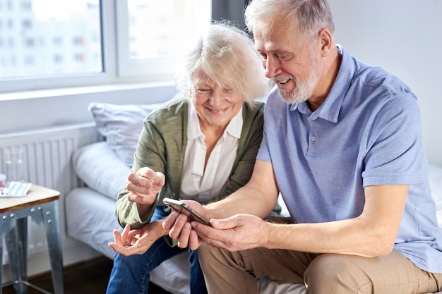 Senior couple looking at children's photos in smartphone, online surfung Net,modern technology concept. caucasian woman and man using mobile phone share social media together in wellbeing home.