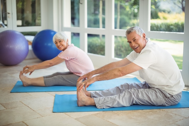 Senior couple performing stretching exercise on exercise mat