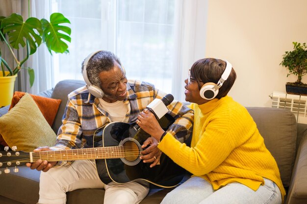 Senior couple playing the guitar and singing together in their living room enjoying their free time Concept retirement music entertainment