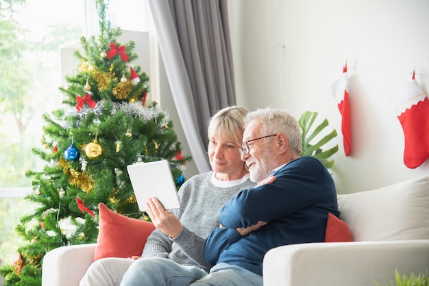 Senior couple sat and looked at tablet in the living room with a Christmas tree