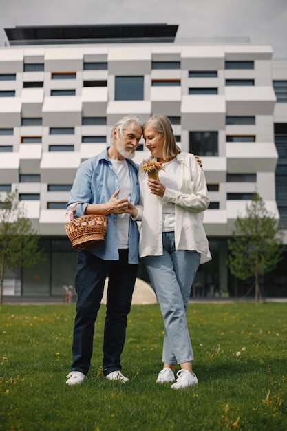 Senior couple standing on a grass in summer with straw basket and flowers