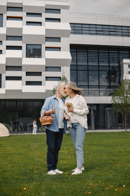 Senior couple standing on a grass in summer with straw basket and flowers