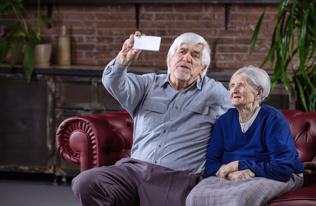 Senior couple taking selfie with smart phone while sitting on couch at home