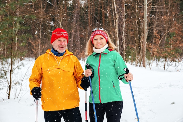 Senior couple walking with nordic walking poles in snowy winter park