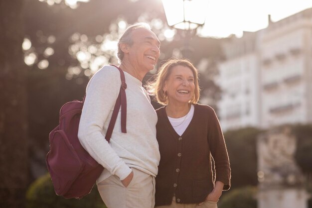 Senior couple with backpack embracing posing near residential building outdoor