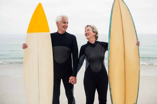 Senior couple with surfboard holding hand on the beach