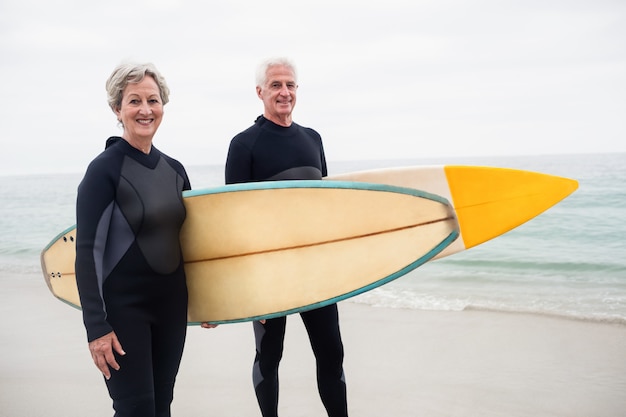 Senior couple with surfboard standing on the beach