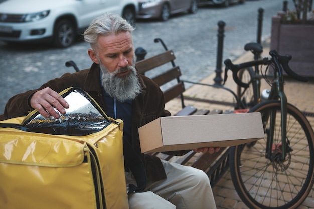 Senior delivery guy putting box package into his backpack