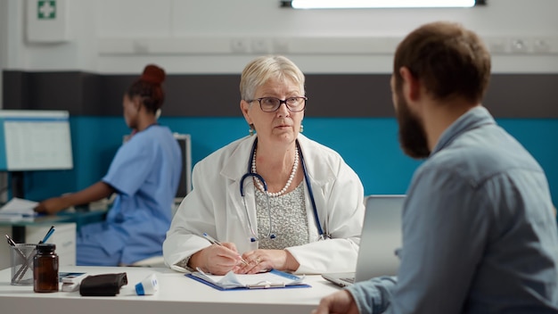 Senior doctor writing consultation information on checkup report to receive treatment from health care system. Prescription medicine on paperwork documents to treat diagnosis.