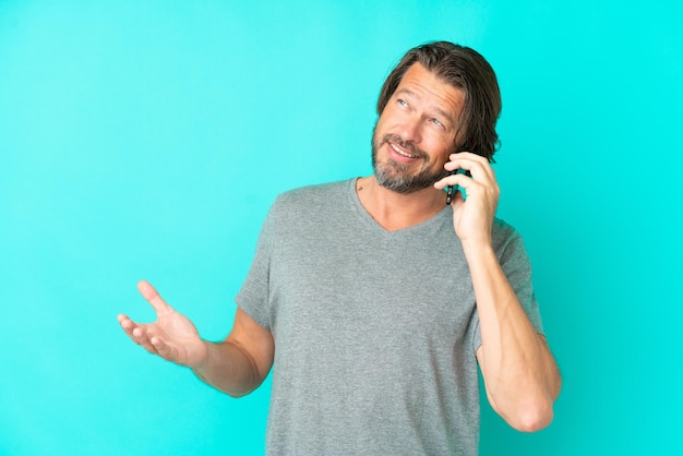 Senior dutch man isolated on blue background keeping a conversation with the mobile phone with someone