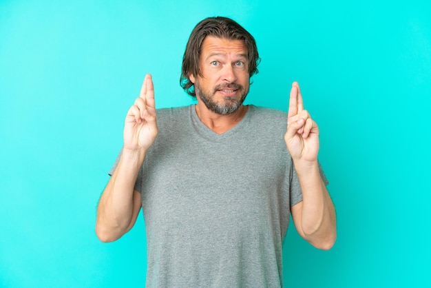 Senior dutch man isolated on blue background with fingers crossing and wishing the best