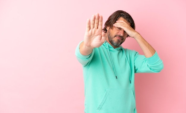 Senior dutch man isolated on pink background making stop gesture and covering face