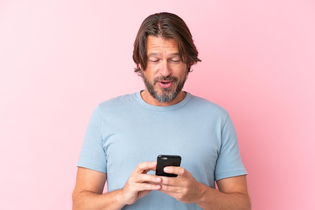 Senior dutch man isolated on pink background sending a message or email with the mobile