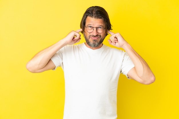 Senior dutch man isolated on yellow background frustrated and covering ears