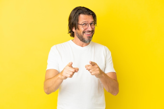 Senior dutch man isolated on yellow background surprised and pointing front