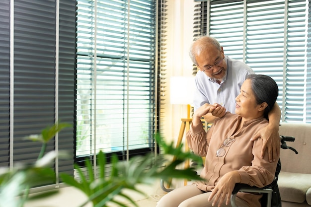 Senior Elderly Couple hold hands together after retirement Husband wife person take care each other in romantic time with smile happy enjoy Asian grandparent sit on wheel chair looking copy space