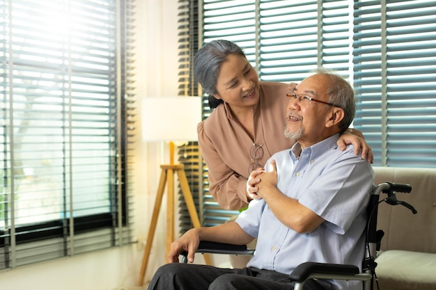 Senior Elderly Couple hold hands together after retirement Husband wife person take care each other in romantic time with smile happy enjoy Asian grandparent sit on wheel chair looking copy space