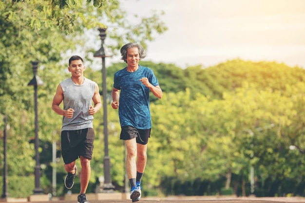 Senior elderly man and a young man running together along the walk path in the park