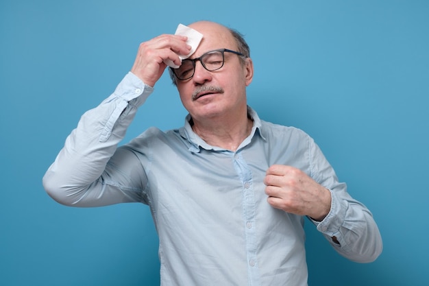 Senior employee sweating in a warm office wiping a forehead