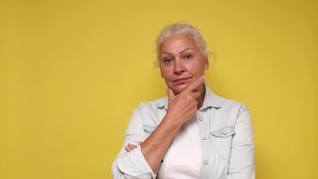 Senior European woman is lost in thought dreaming and scratching her chin with her finger