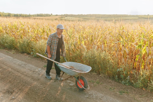 Senior farmer pushing wheelbarrow on country road near field