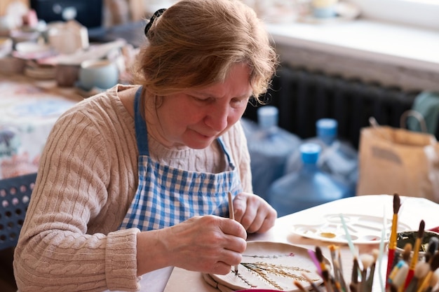 Senior female artist making flower ornament on ceramic product