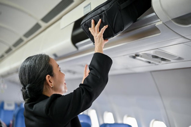 A senior female passenger is putting her luggage in an overhead locker before takeoff