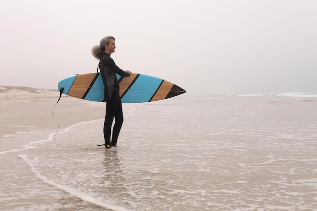 Photo senior female surfer with surfboard standing on the beach