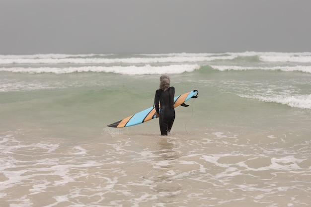 Photo senior female surfer with surfboard standing in the sea