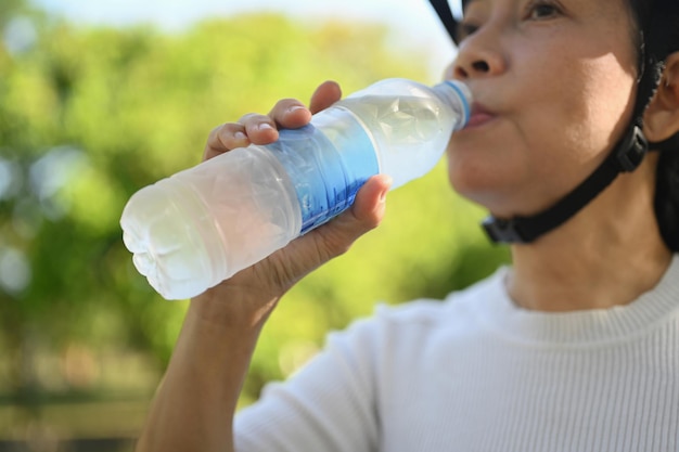 Senior fitness woman drinking water from a bottle resting after riding bicycle in park