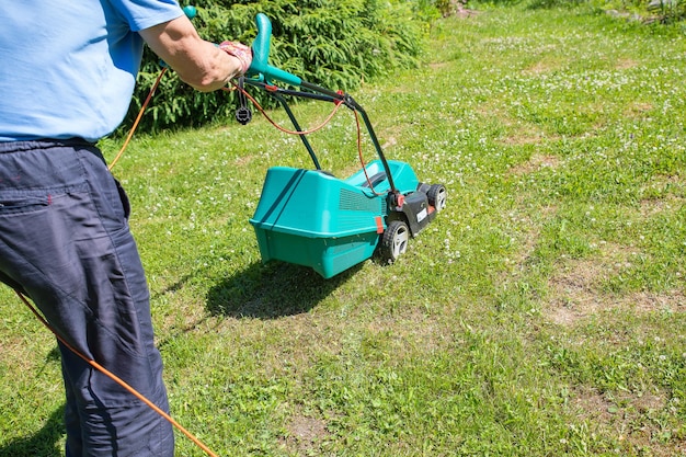 Senior gardener mowing his green lawn in garden Man working on lawn cutting grass with lawn mower man is mowing grass with an electric mower Physical labor and parttime work