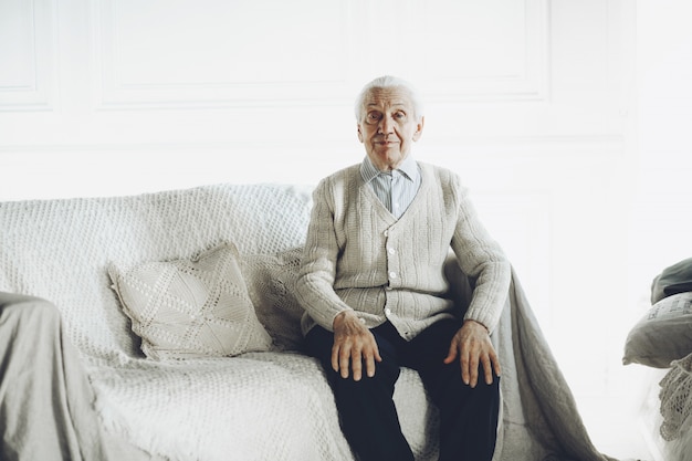 Senior gentleman sitting on modern sofa looking at camera