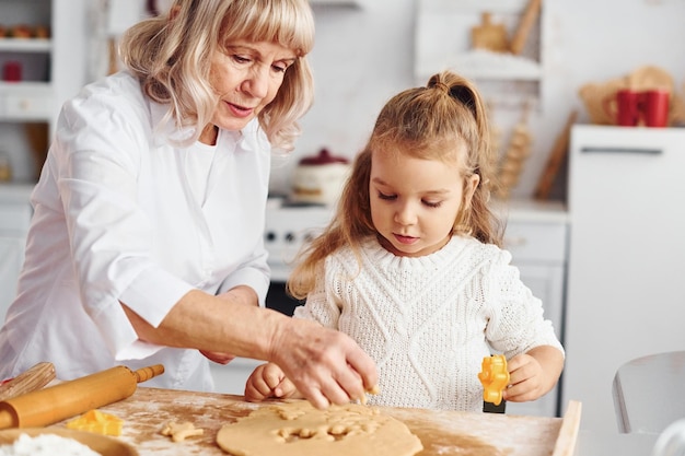 Senior grandmother with her little granddaughter cooks sweets for Christmas on the kitchen