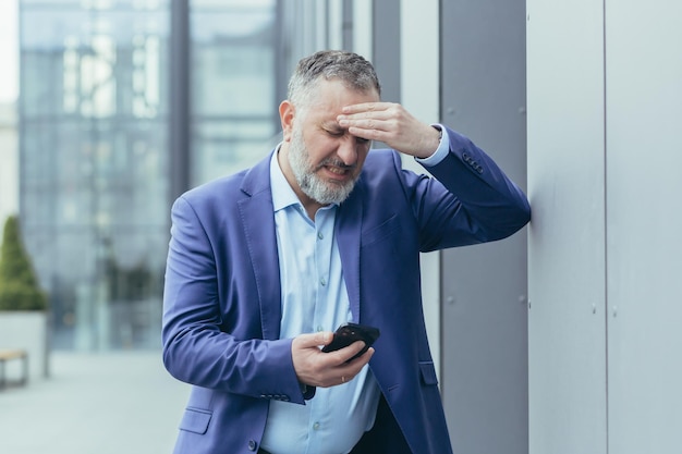 Senior grayhaired businessman sick outside office building man holding hand to head having severe