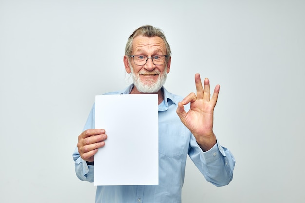 Senior greyhaired man in a blue shirt and glasses a white sheet of paper cropped view